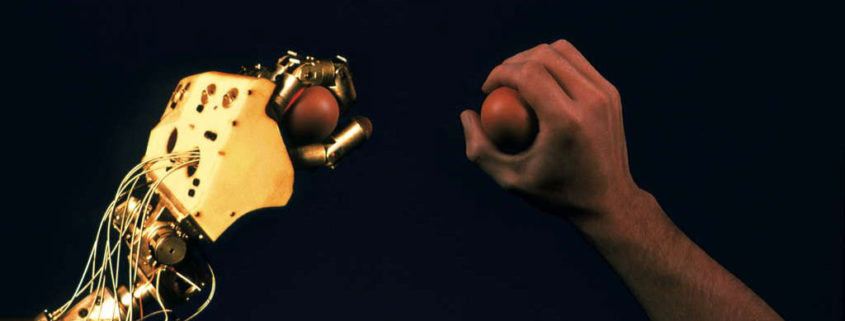 Una mano umana e una bionica stringono una pallina